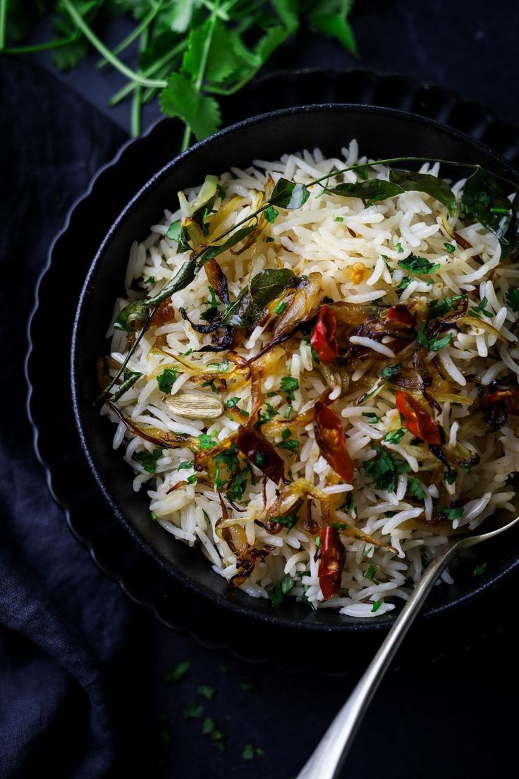 a skillet filled with rice and vegetables on top of a black cloth next to some parsley