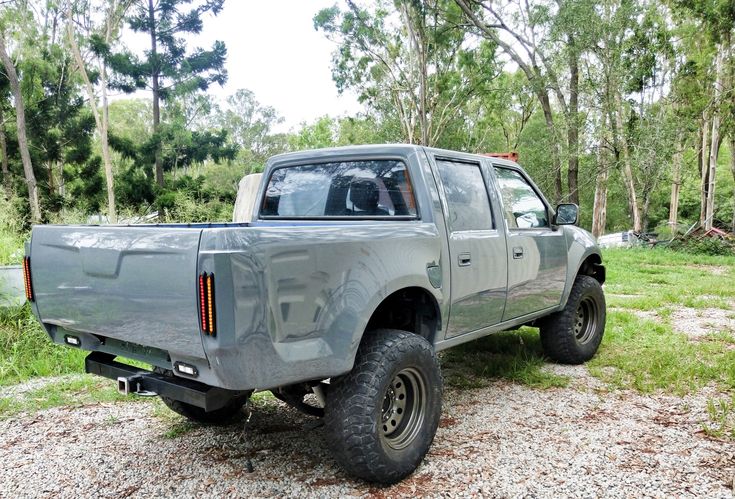 a pick up truck parked in the middle of a field with trees and grass behind it