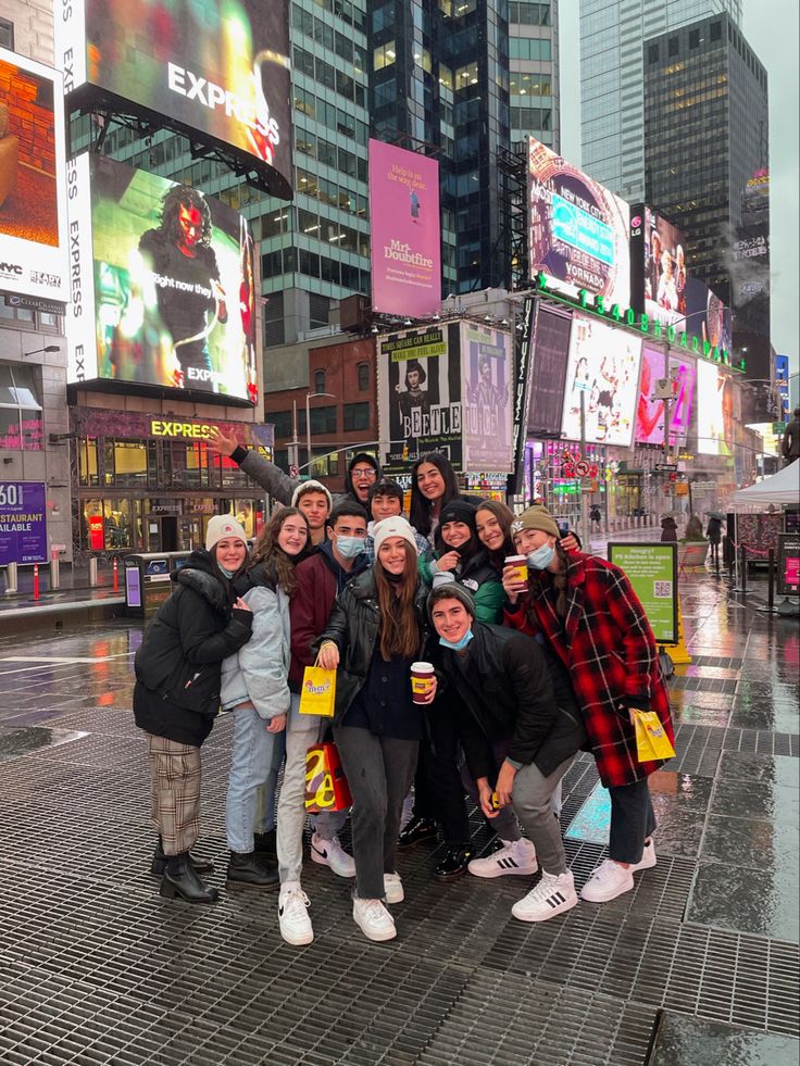 a group of people posing for a photo in times square on a rainy day with their faces covered by masks