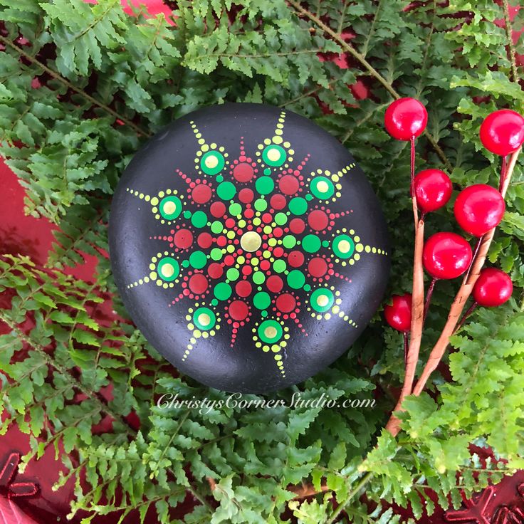 a painted rock surrounded by green plants and red berries on the planter's side