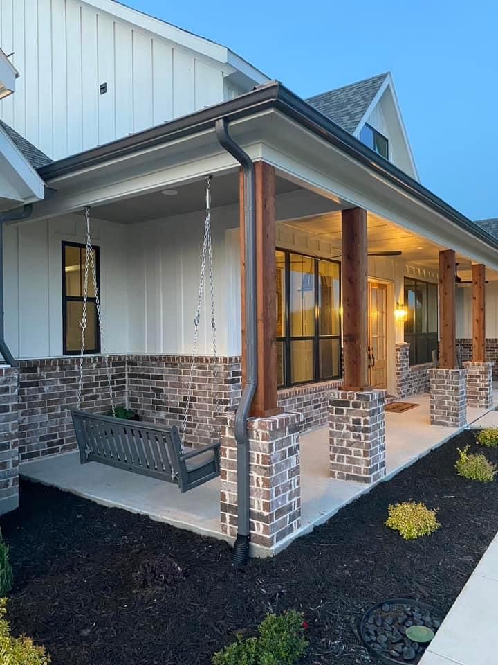 the front porch of a home with swings and chairs on the lawn at night time