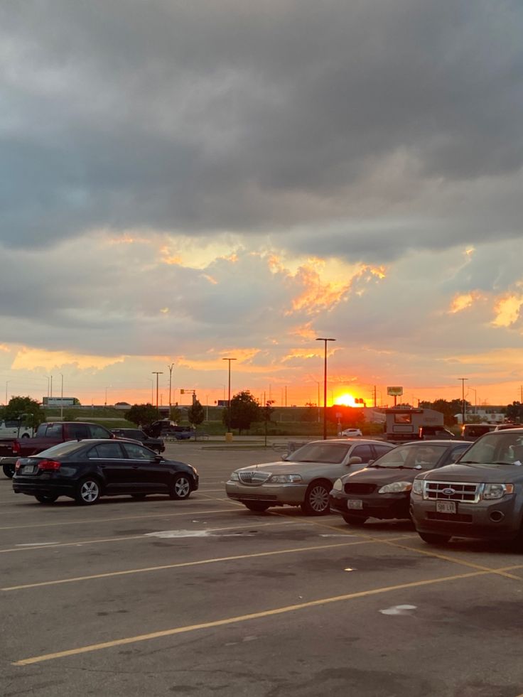 a parking lot filled with lots of parked cars under a cloudy sky at sunset or sunrise