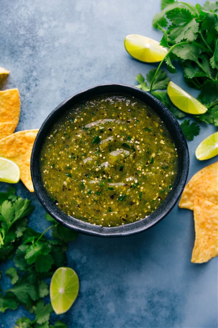 a black bowl filled with salsa surrounded by cilantro, limes and tortilla chips