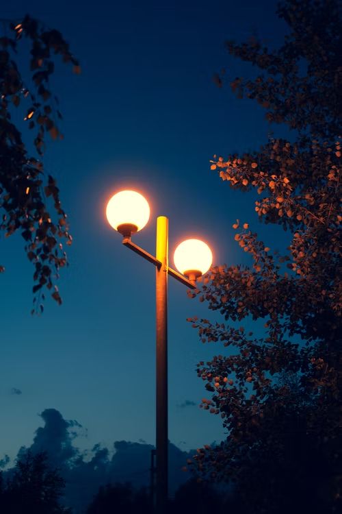 two street lights are lit up in the night sky with trees and clouds behind them