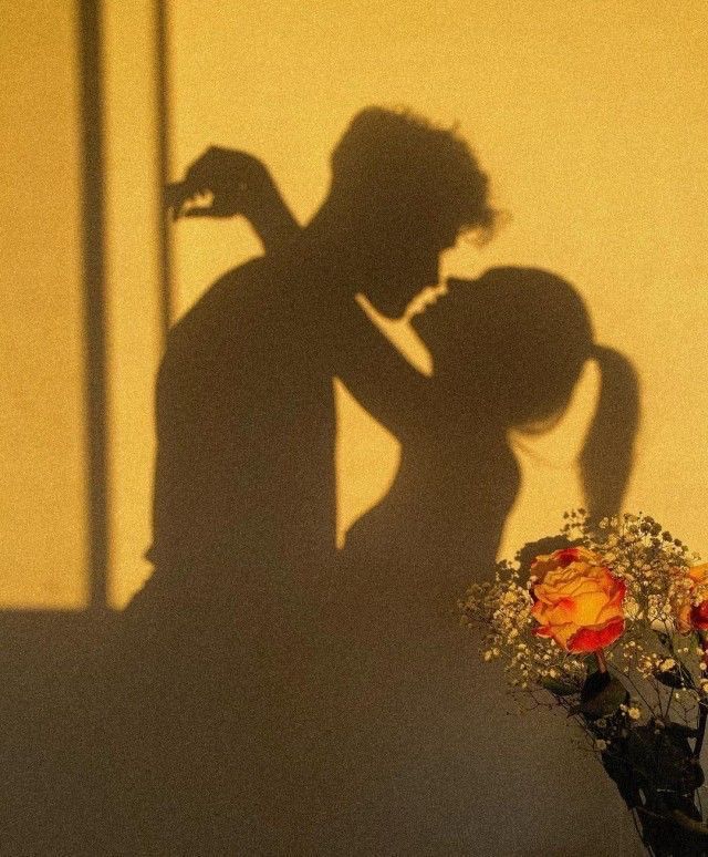 the shadow of a man and woman kissing in front of a wall with flowers on it