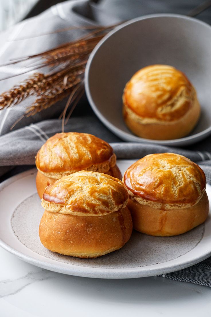 three pastries sitting on a plate next to a bowl with wheat stalks in it