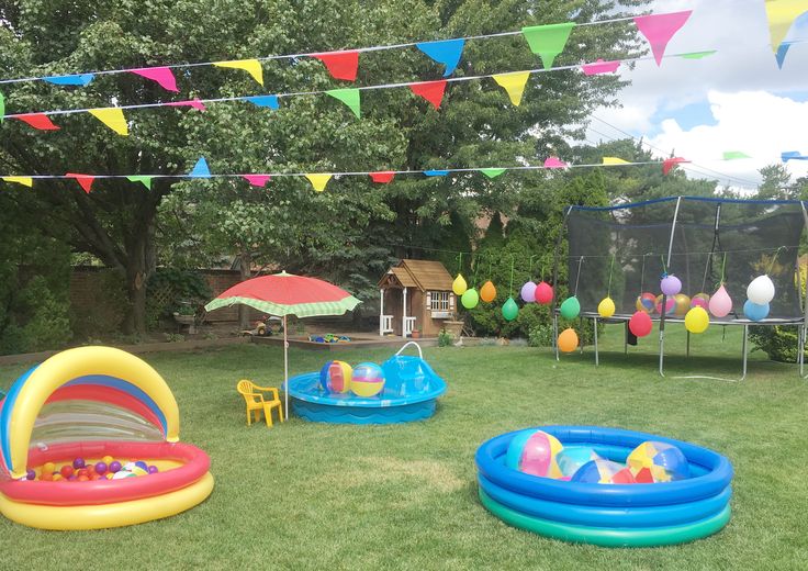 an inflatable pool and other toys are on the grass near bunting flags