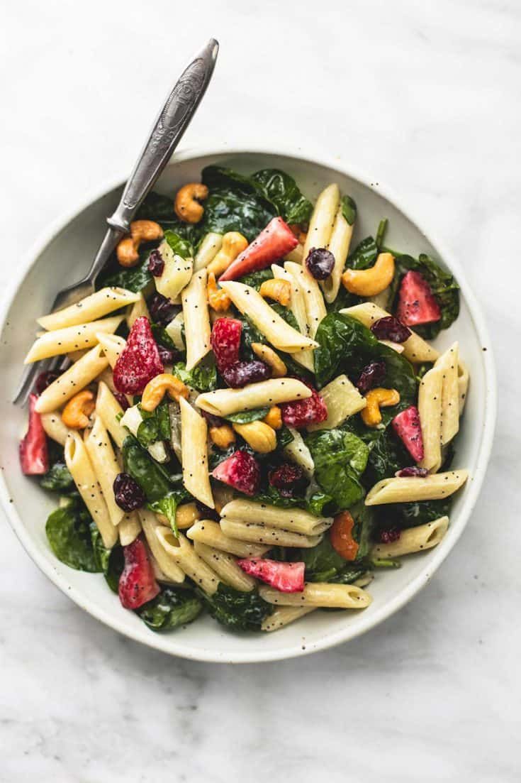 a white bowl filled with pasta, strawberries and spinach on top of a marble table