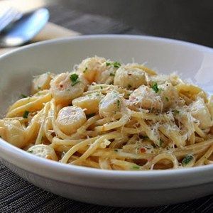 a white bowl filled with pasta covered in shrimp and parmesan cheese on top of a wooden table