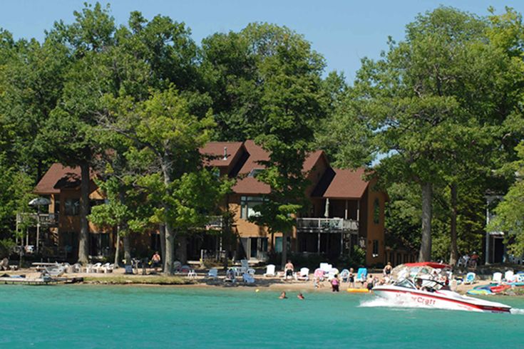 a boat is in the water next to a large house with lots of trees around it