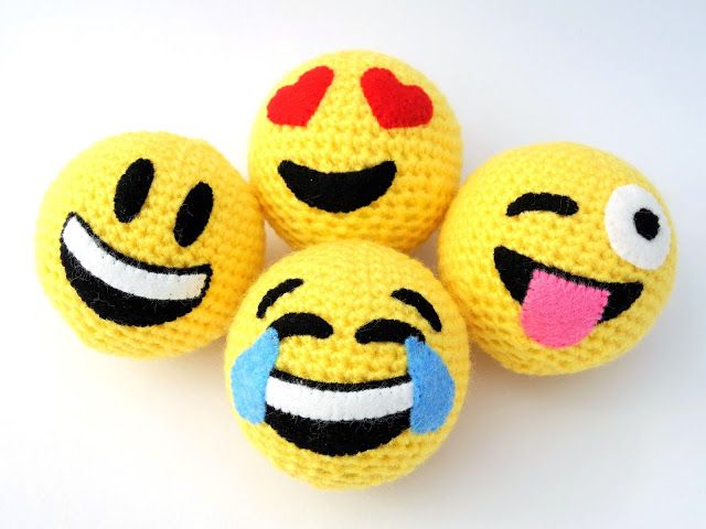 four yellow crocheted smiley face balls with red eyes and mouth, on a white background