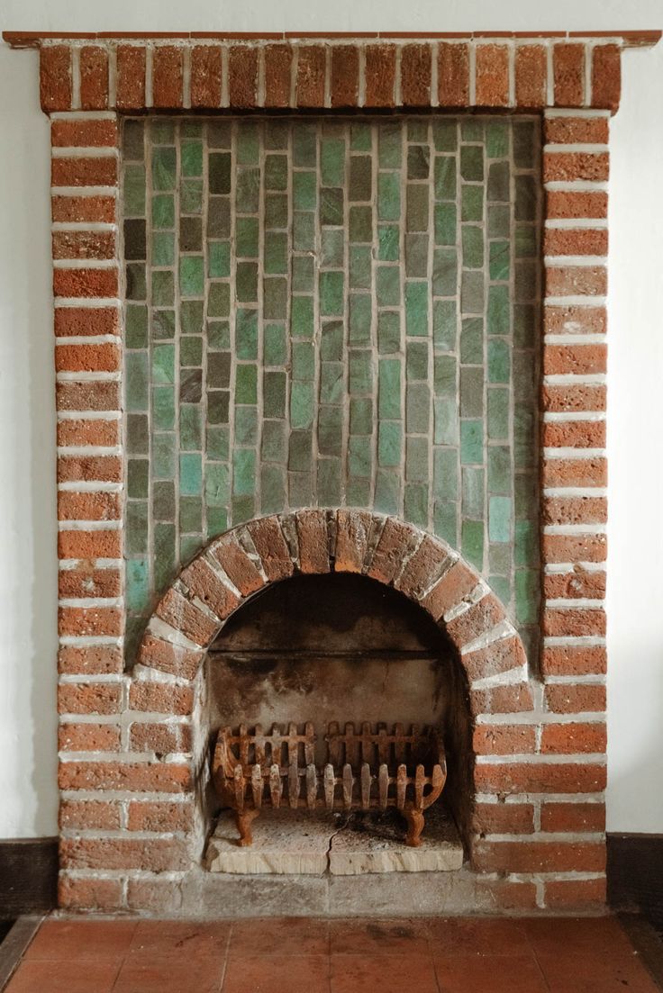 an old brick fireplace in a room with tile flooring and green tiles on the wall