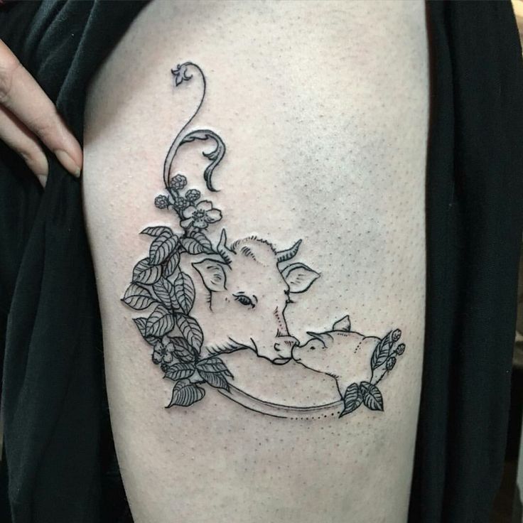 a woman's thigh with a cow and flowers tattoo on her side, while the calf is laying down