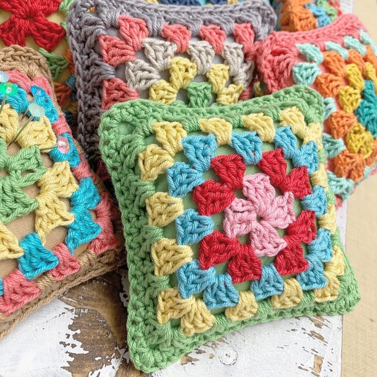 four crocheted square pillows sitting on top of a wooden table next to each other