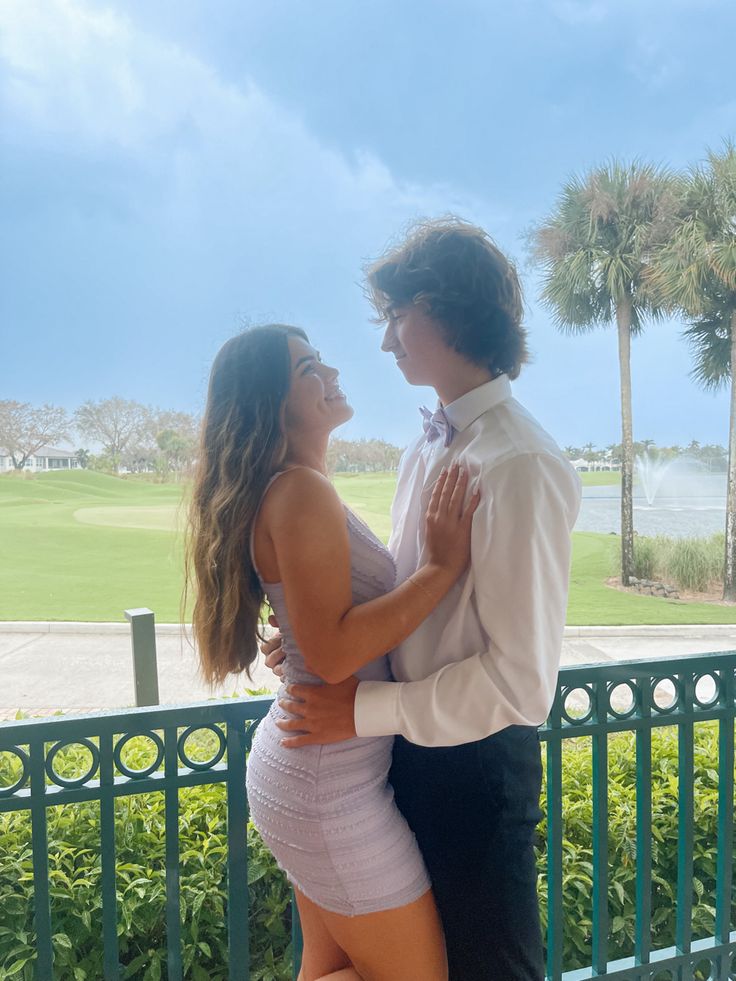 a man and woman standing next to each other in front of a green fence with palm trees