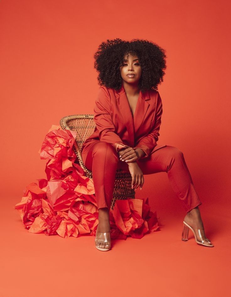 a woman sitting on top of a chair wearing a red suit and high heel shoes