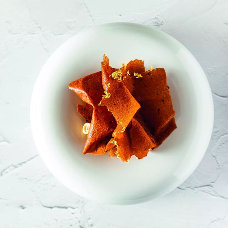 a white bowl filled with pieces of food on top of a wooden table next to a wall