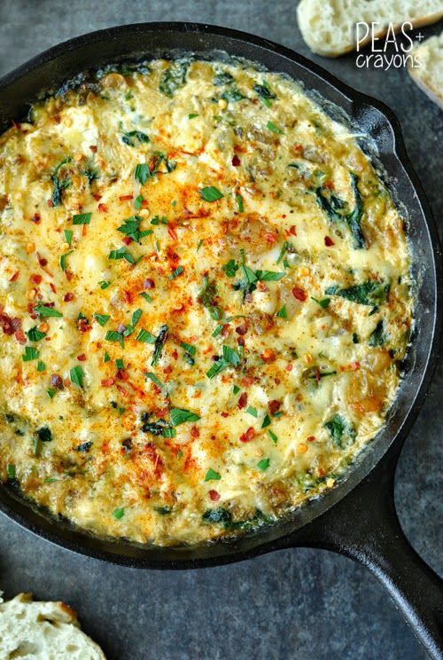 a skillet filled with cheese and spinach on top of a table next to slices of bread