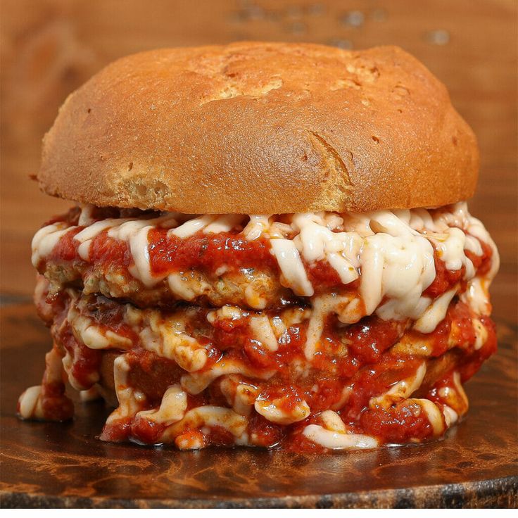 a close up of a sandwich with meat and sauce on a wooden board next to bread