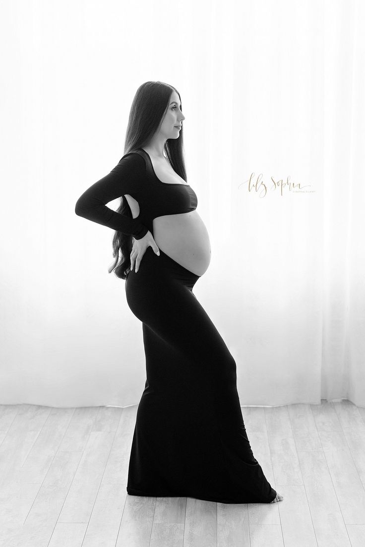 a pregnant woman in a long black dress poses for a photo with her hands on her hips