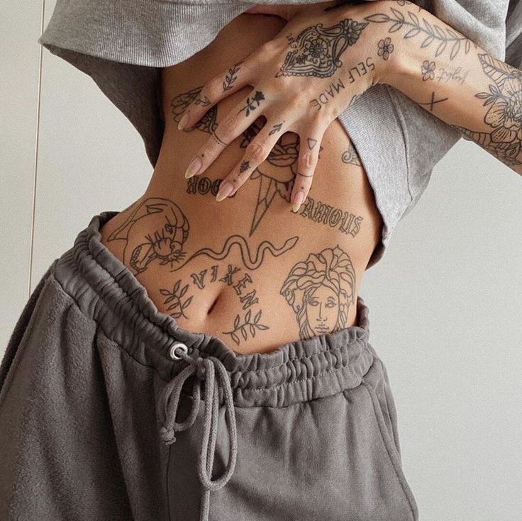 a woman with tattoos on her stomach wearing sweatpants and a hoodie sweatshirt, holding her hands behind her back