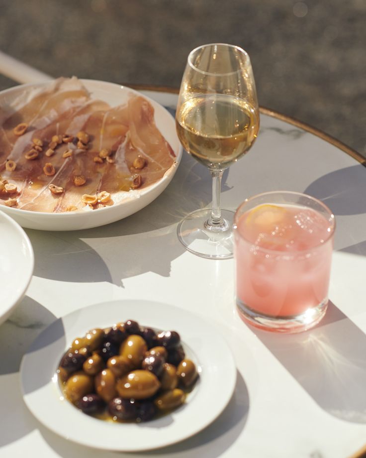 a table topped with plates and bowls filled with food next to glasses of wine on top of it