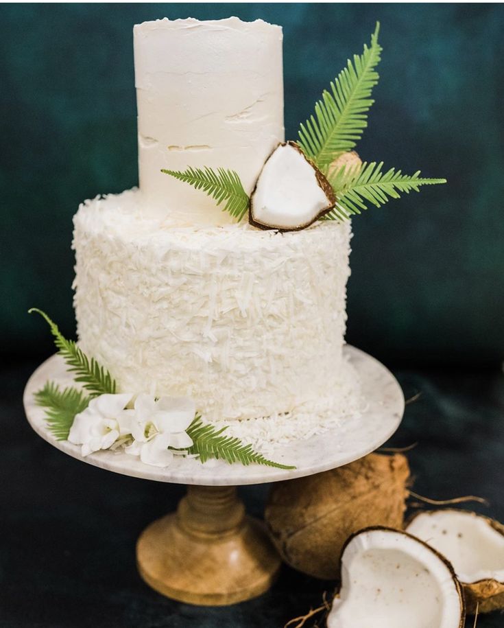 a white cake with coconuts next to it on a plate and green leafy decoration