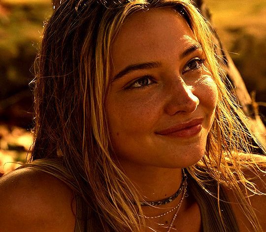 a beautiful young woman sitting next to a tree