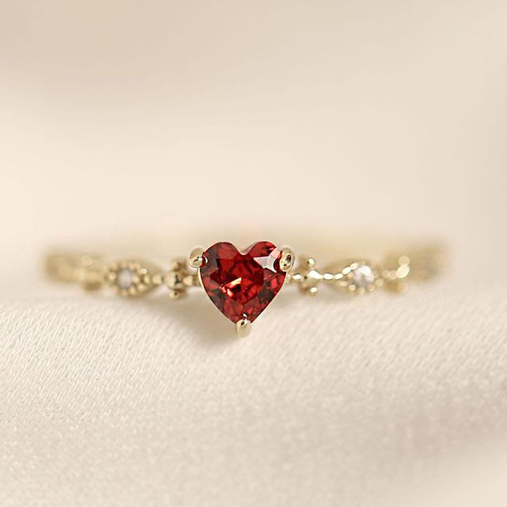 a red heart shaped ring sitting on top of a white cloth