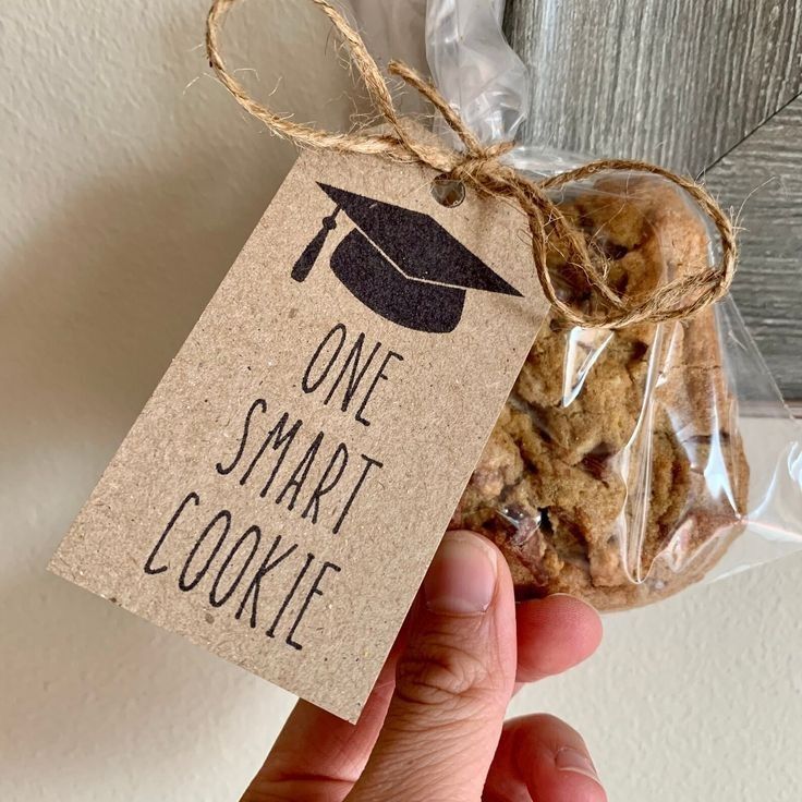 a hand holding a tag that says one smart cookie with a graduation cap on it