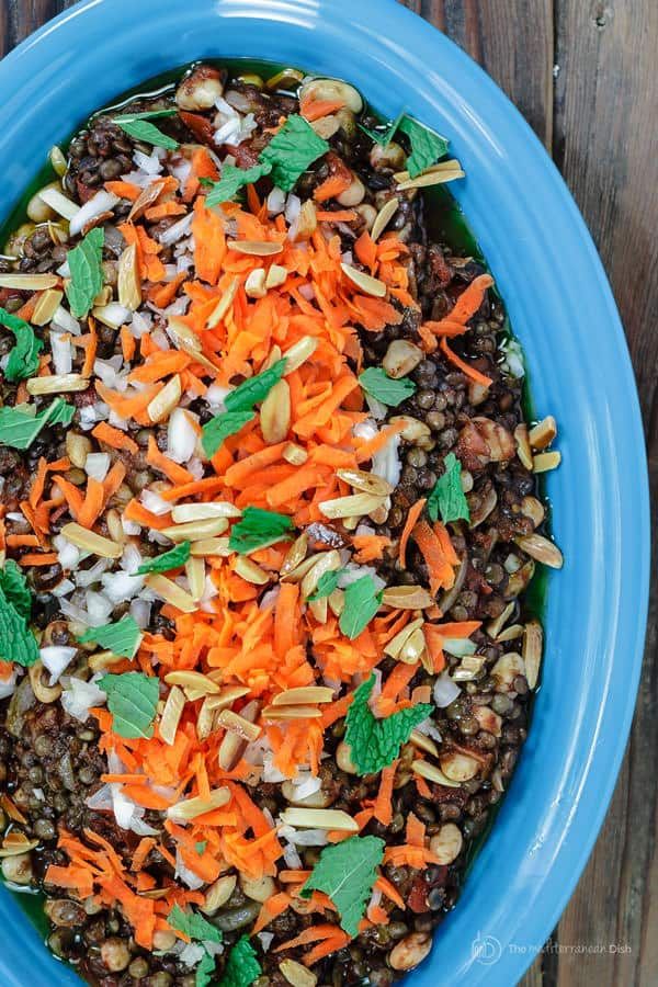 a blue bowl filled with carrots, lentils and other vegetables on top of a wooden table