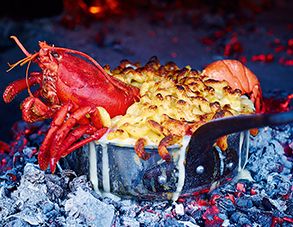 lobsters and macaroni being cooked in an outdoor oven with flames behind them