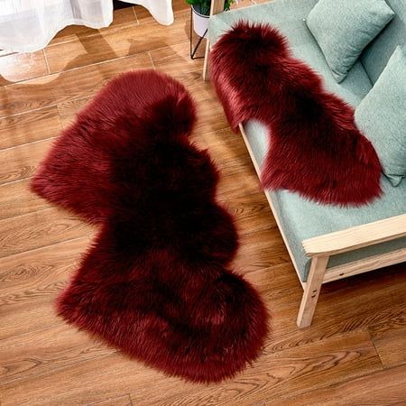 two red fur rugs sitting on top of a wooden floor next to a couch