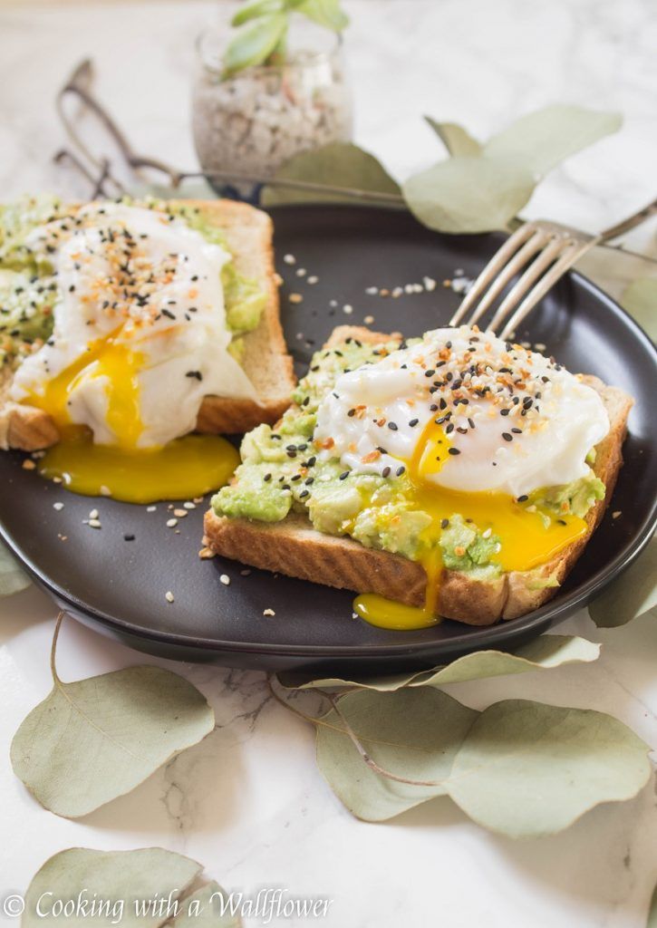 two pieces of toast with avocado and poached eggs on them sitting on a black plate