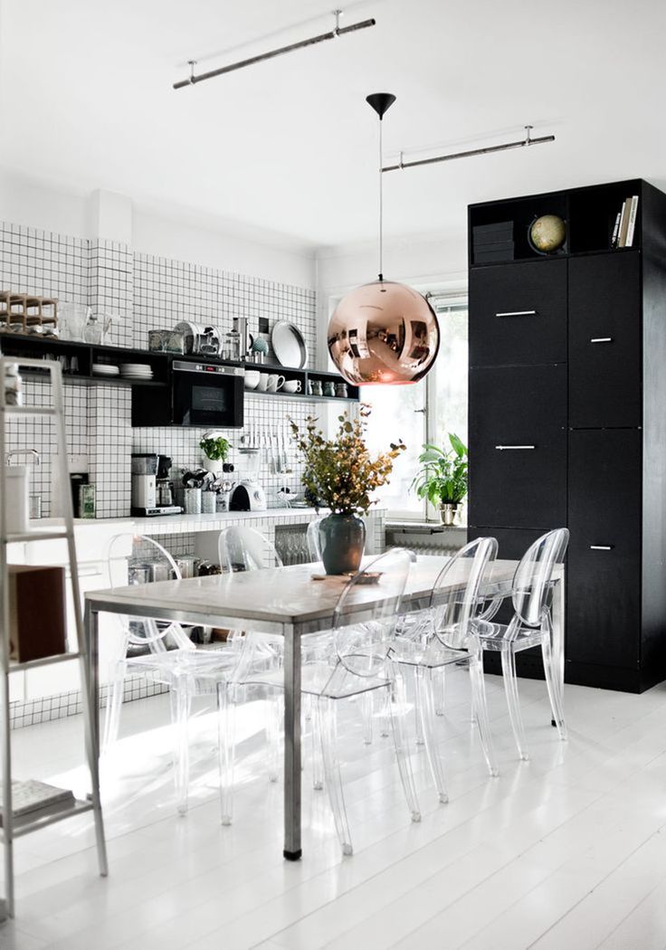 a dining room table surrounded by clear chairs and an open kitchen area with black cabinets