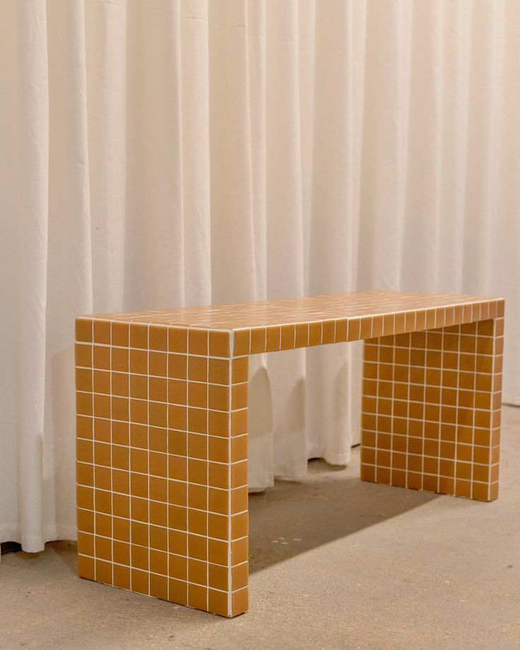 a yellow bench sitting in front of a white curtain