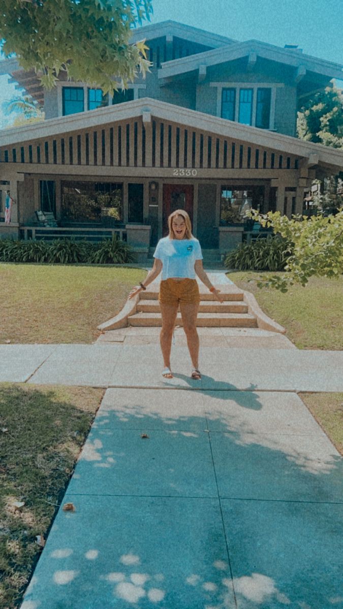 a woman standing in front of a house with her arms out and legs spread wide