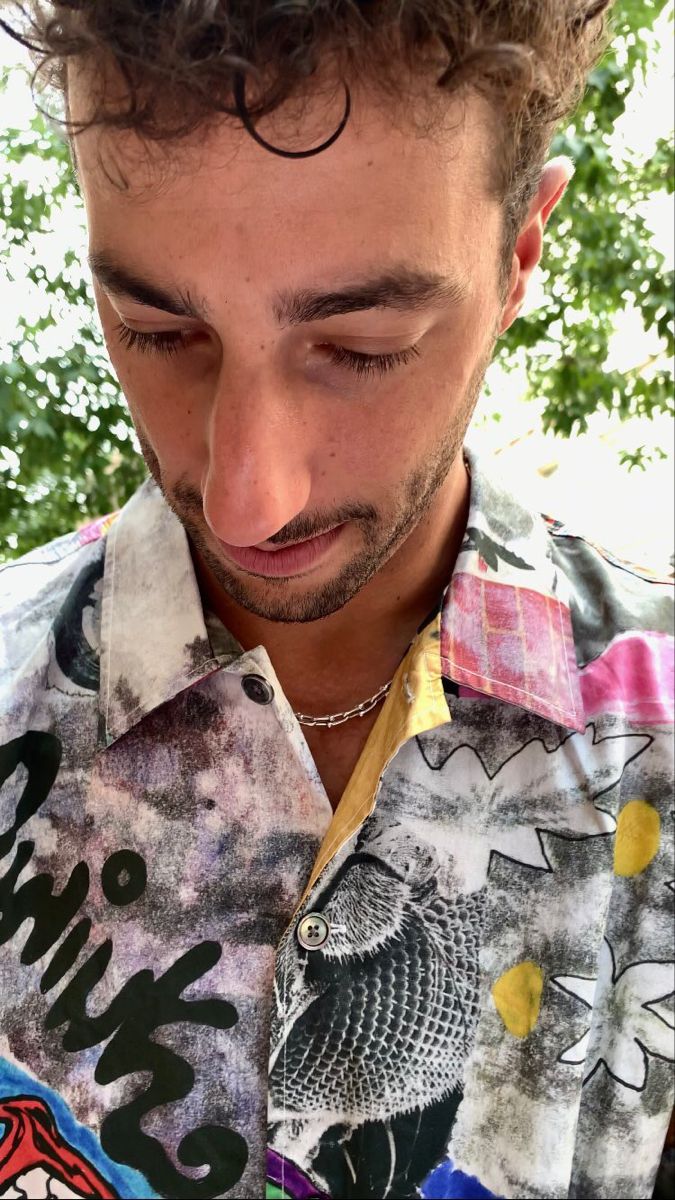 a man with curly hair looking down at his cell phone while wearing a colorful shirt