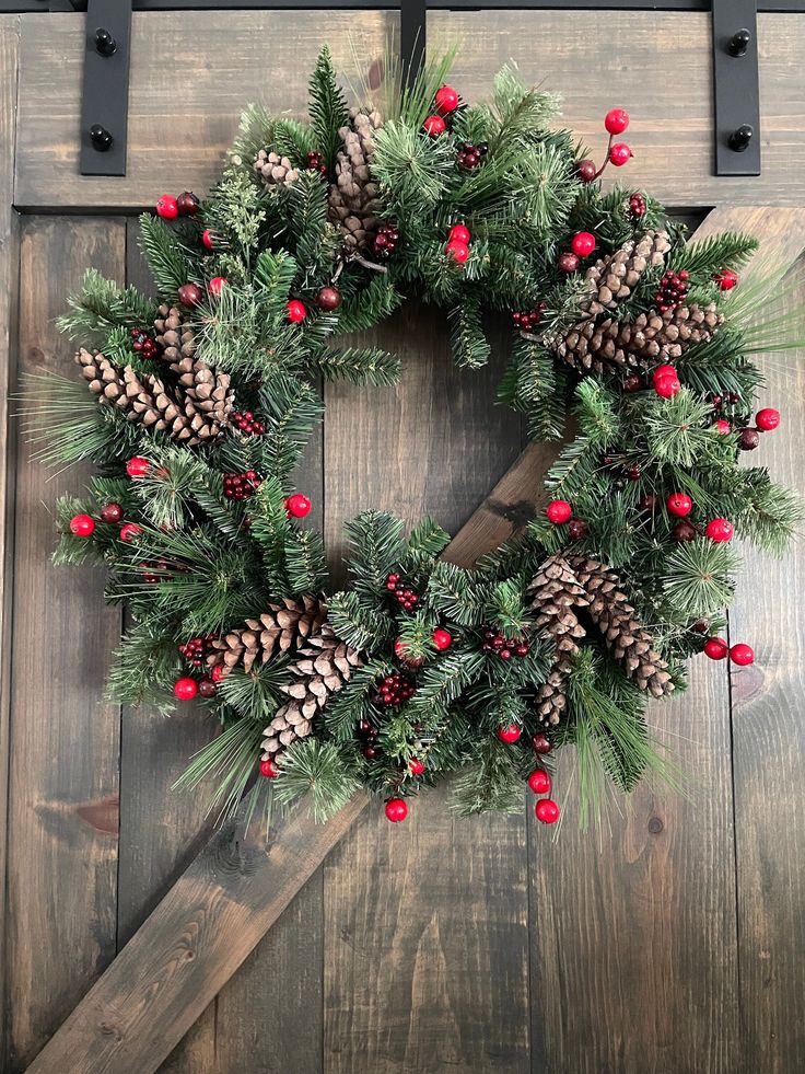 a wreath with pine cones and red berries hangs on a wooden door frame in front of a barn door