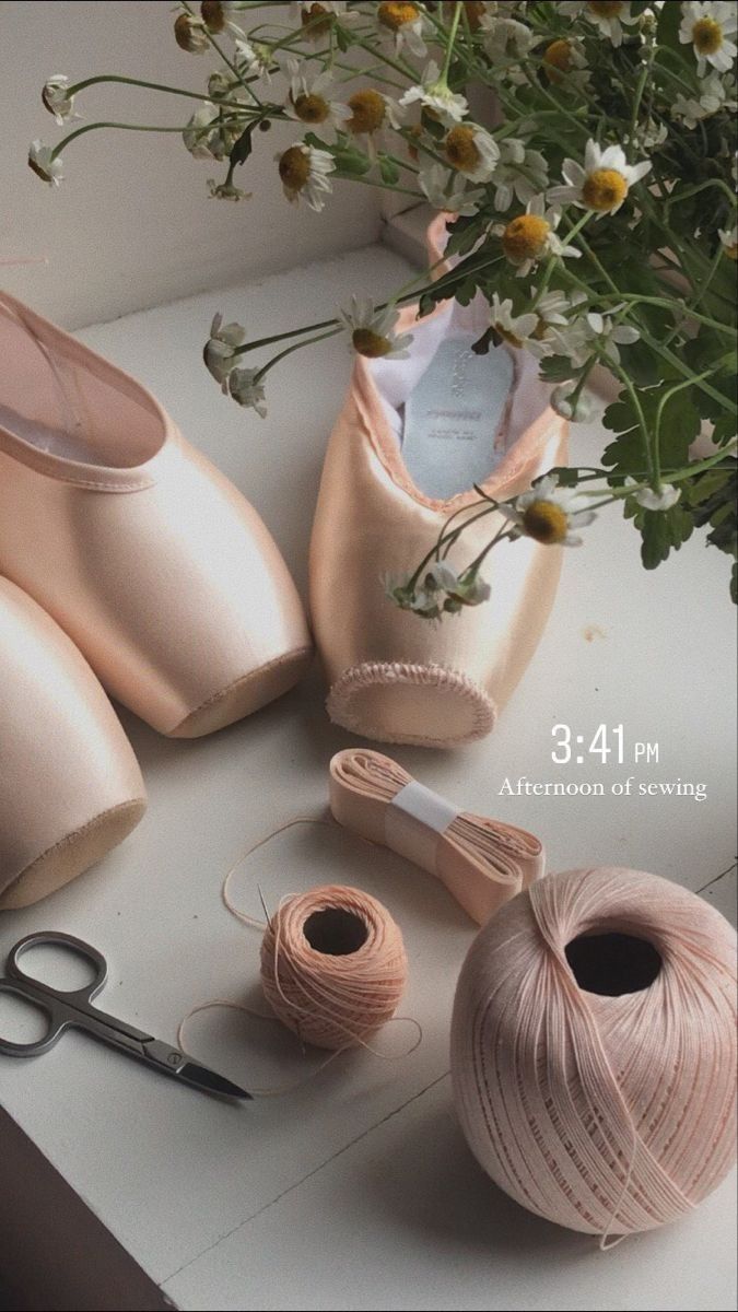 a pair of pink ballet shoes sitting on top of a table next to yarn and flowers