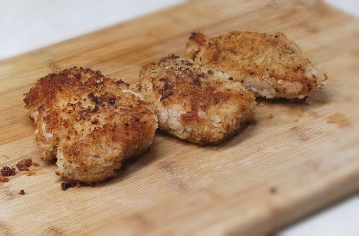 two pieces of chicken sitting on top of a wooden cutting board