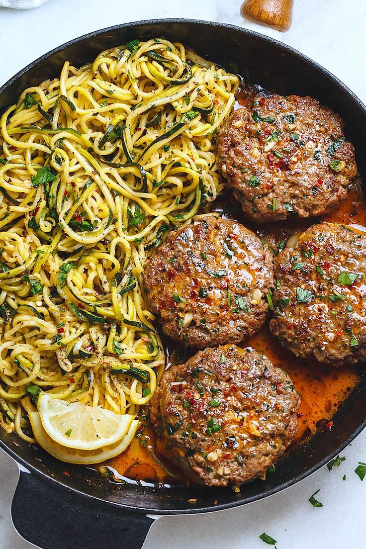 meatballs and noodles in a skillet with lemon wedges on the side for garnish