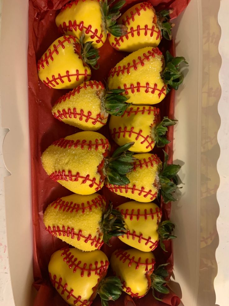 strawberries with yellow and red baseballs in a white box on top of a table