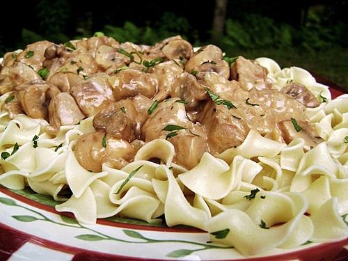 a plate full of pasta with meatballs and sauce on the tablecloth in front of some trees