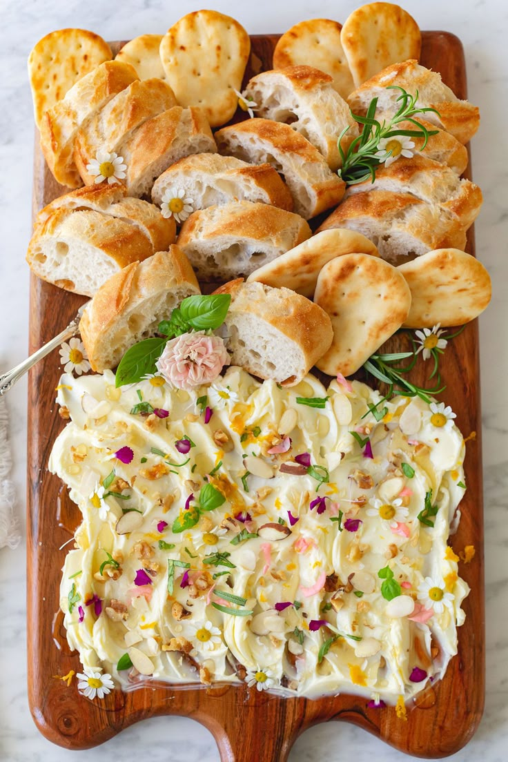 a wooden platter with bread and crackers on it next to a bowl of coleslaw