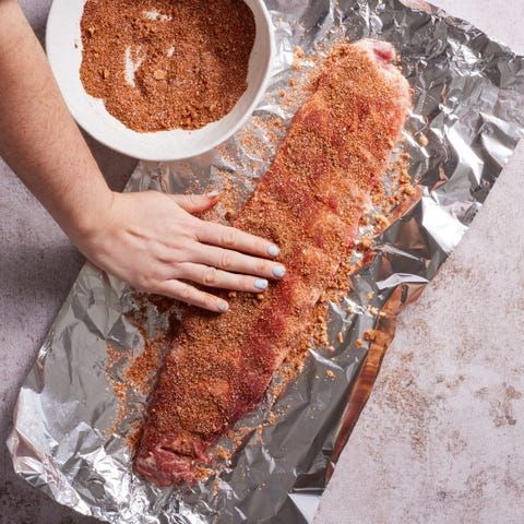 a person is holding a large piece of meat on tin foil with seasoning in it