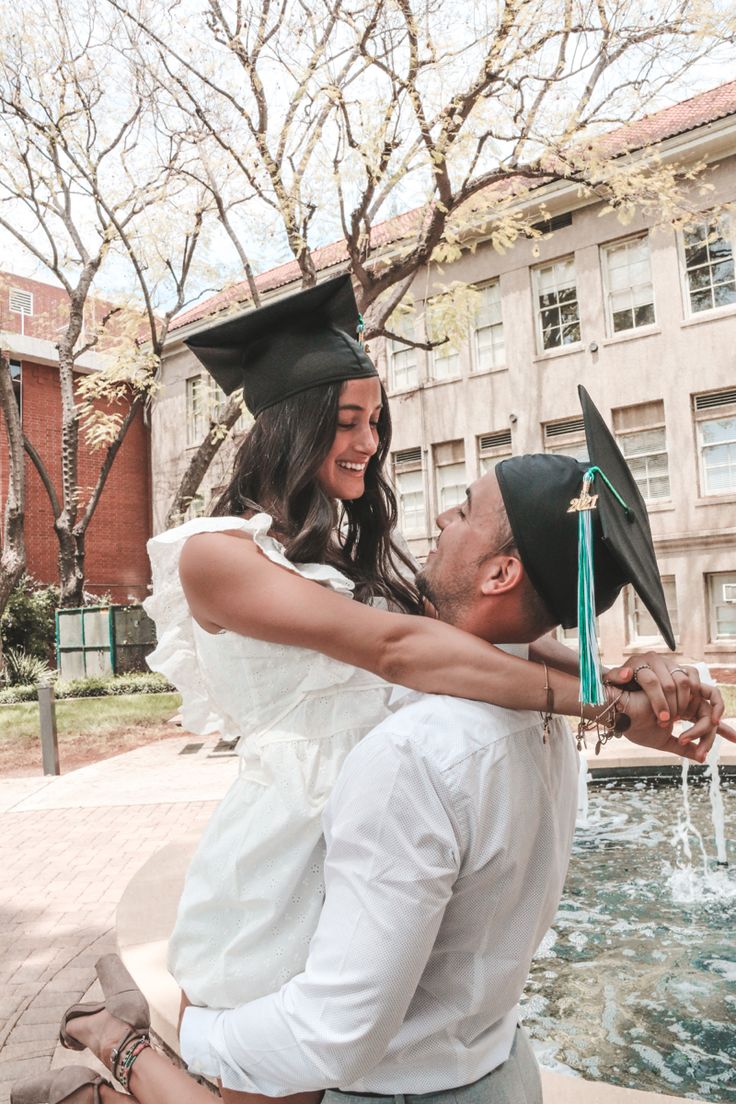 a man holding a woman in his arms while she is wearing a graduation cap and gown