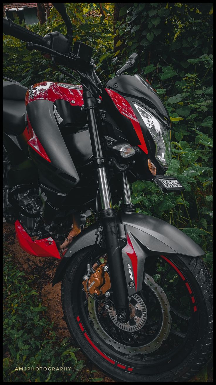 a red and black motorcycle parked on the side of a road in front of some trees