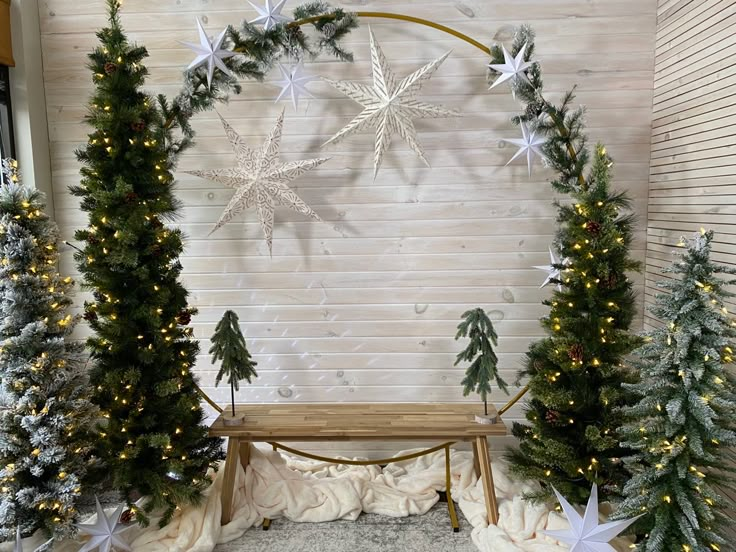 a wooden bench surrounded by christmas trees and lights in front of a white brick wall