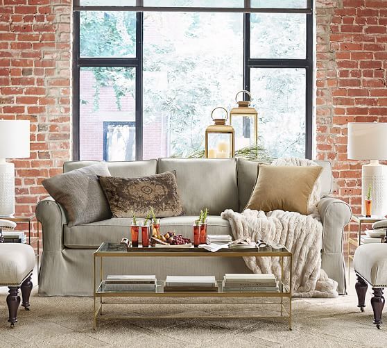 a living room filled with lots of furniture next to a large window and brick wall